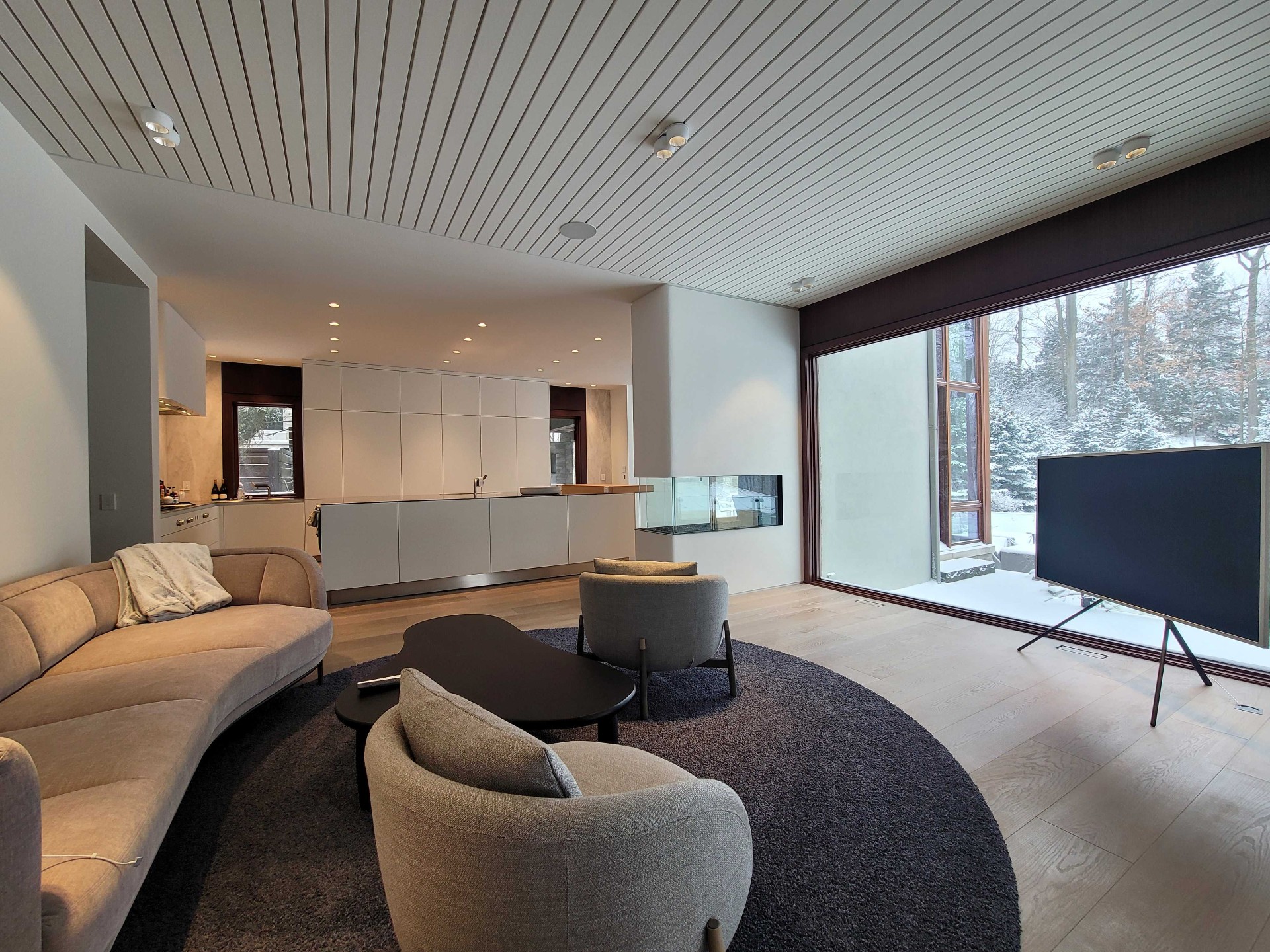 Modern living room with easel-style TV, linear ceiling and floor-to-ceiling windows