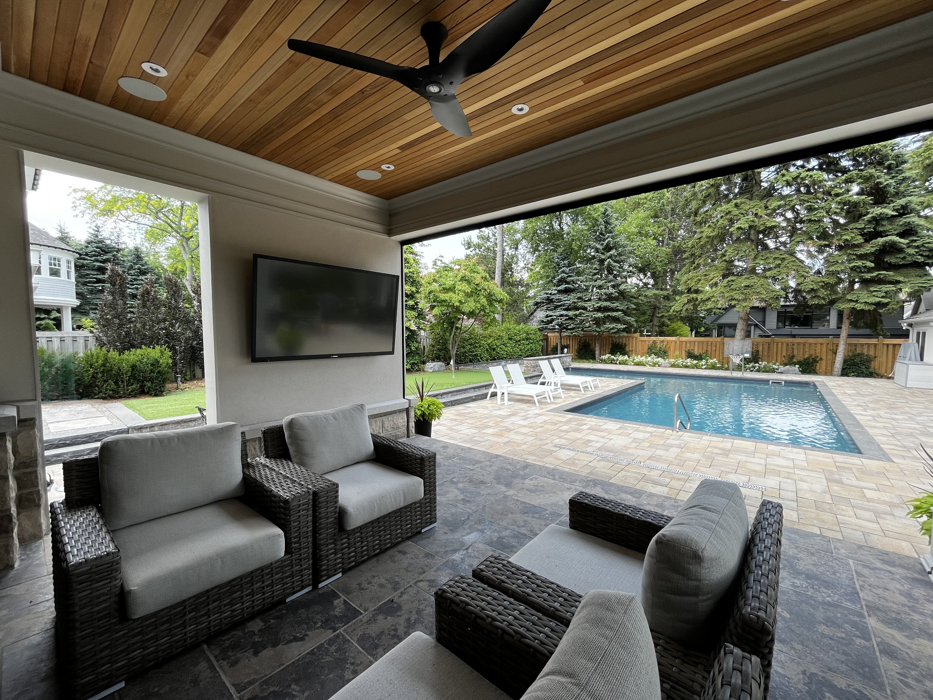 Covered outdoor living space with weatherproof TV, ceiling speakers and poolside view