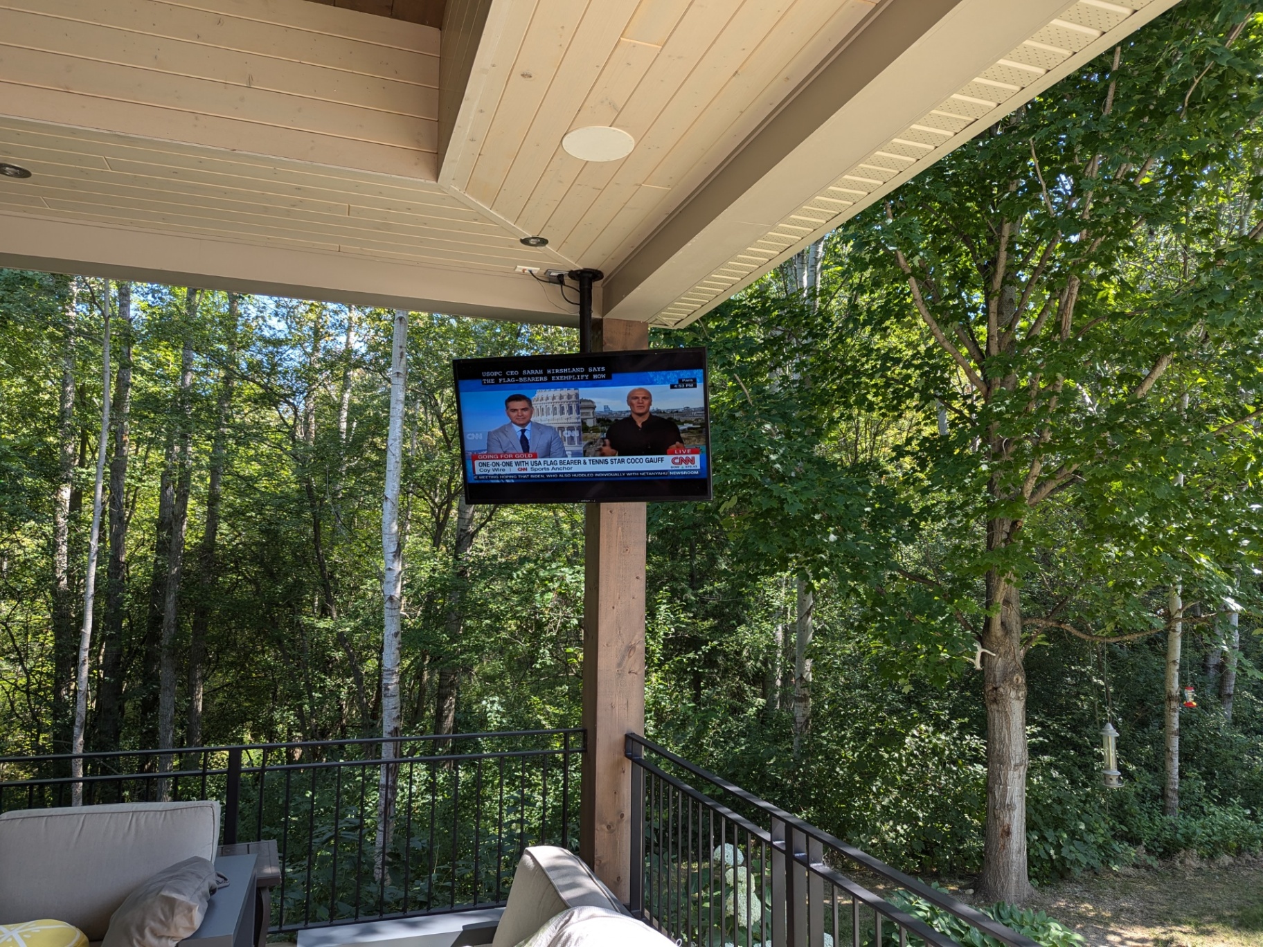 Covered deck with outdoor television overlooking a wooded backyard